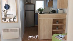 A compact kitchen with a microwave, refrigerator, and wooden cabinets. - Camping 3 étoiles - Piscine  - ccbfidi (Les Moutiers-en-Retz)