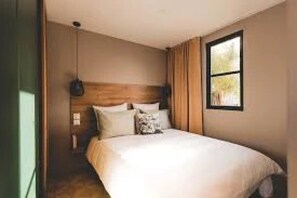 Ein Schlafzimmer mit einem hölzernen Kopfende, einem Bett mit weißer Bettwäsche, einem Nachttisch und einem Fenster mit Ausblick.
