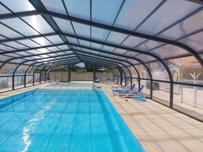 Ein Innenpool mit Glasdecke, blauen Liegestühlen und Fliesenboden.