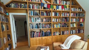 A cozy reading nook with a leather armchair, a small ottoman, and a bookshelf filled with books. - Private Garden Estate, Jacuzzi, Cinema & Games (Southborough)
