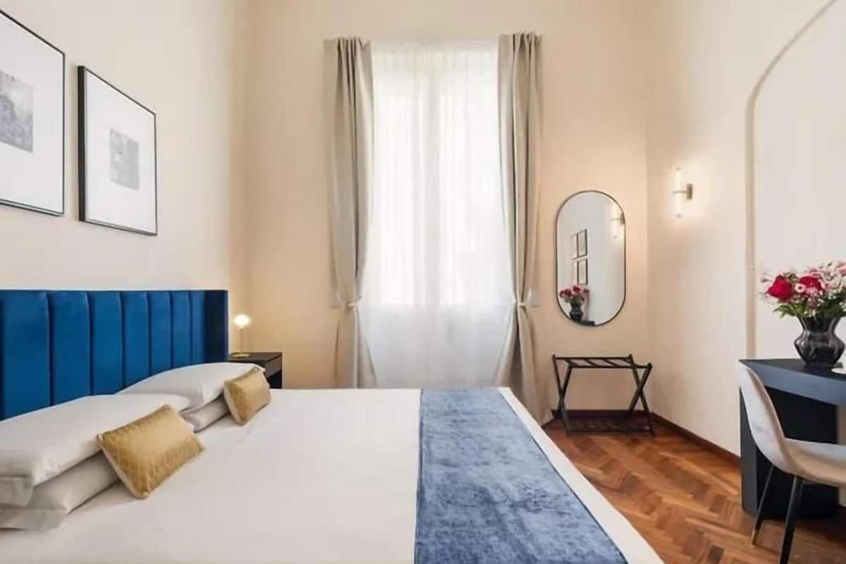 Hotellihuone, jossa on sänky, työpöytä, tuoli, peili ja ikkuna, jossa on verhot.