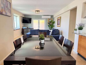 Ein Essbereich mit einem runden Tisch, Stühlen, einem Fernseher, einer Couch und einer Topfpflanze.