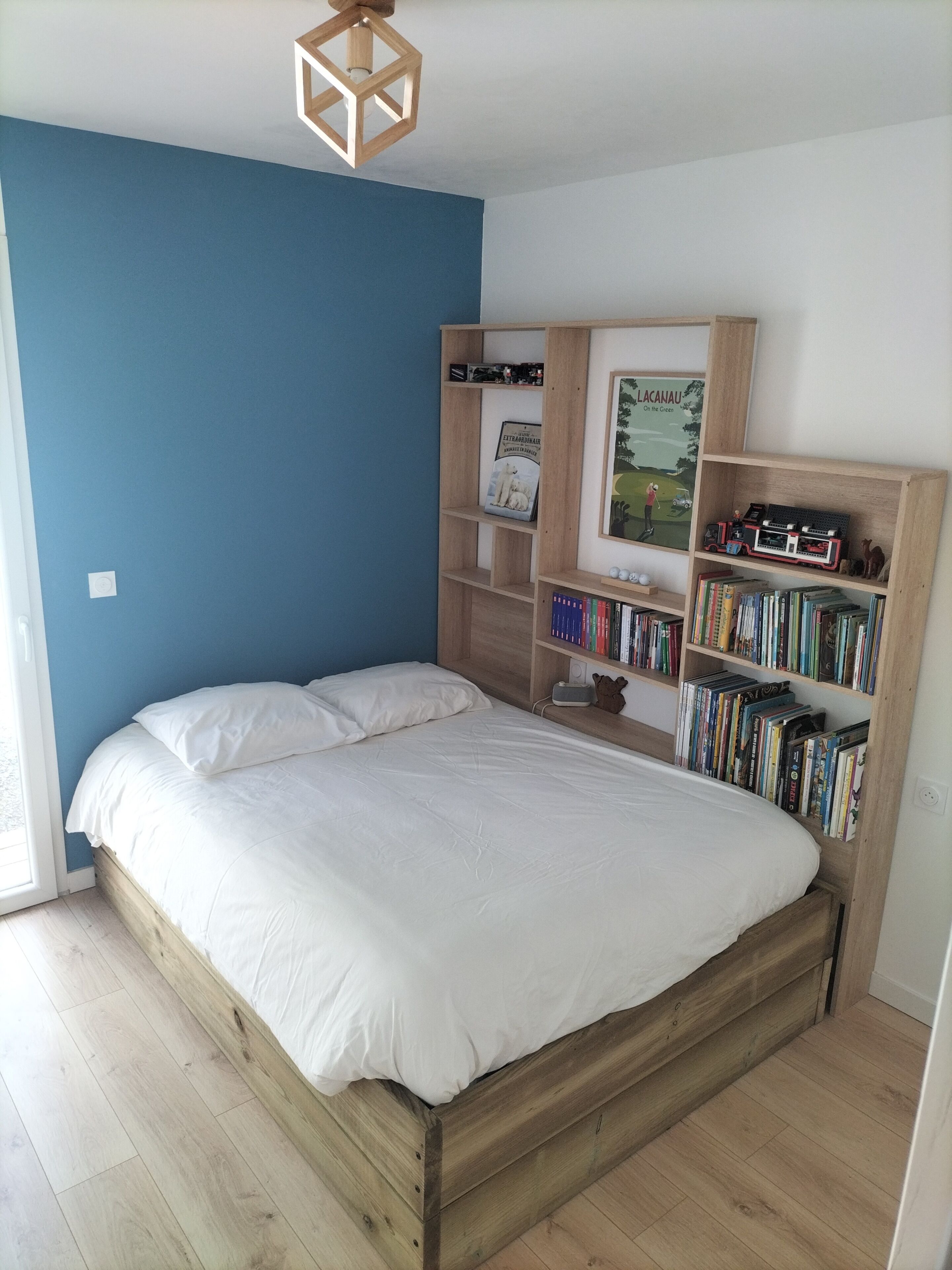 A bedroom with a wooden bed, a bookshelf, and a desk with a computer.