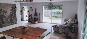 Un vaste espace de vie comprenant une table à manger en bois, un canapé et une grande porte-fenêtre coulissante donnant sur un jardin.