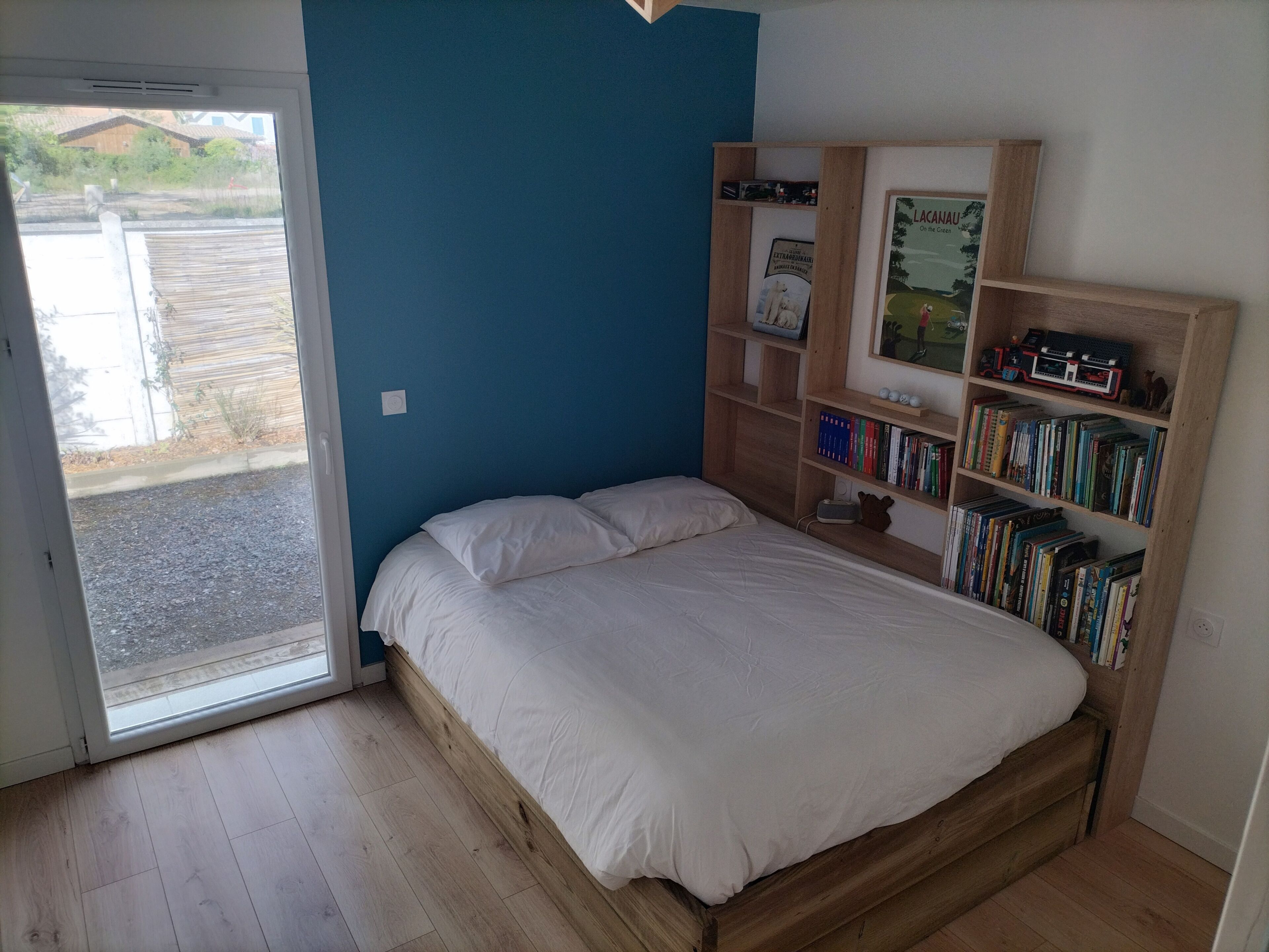 Ein Schlafzimmer mit einem Bett, einem Bücherregal und einer Tür, die auf einen Balkon führt.