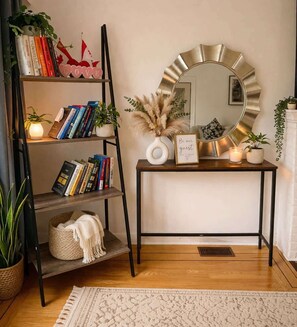 A room with a bookshelf, a console table with a mirror, a framed sign, and a potted plant.