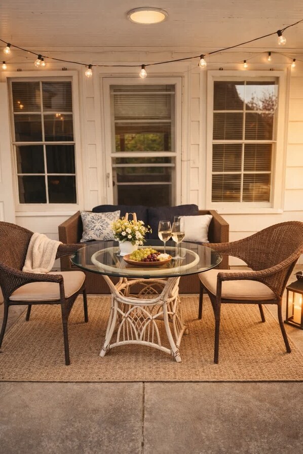 A covered patio with wicker furniture, a glass table, and string lights.