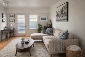 A living room with a sofa, a coffee table, a desk, and a large window with blinds.