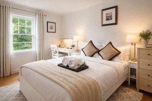 A hotel room with a large bed, a desk, two lamps, and a window with curtains.