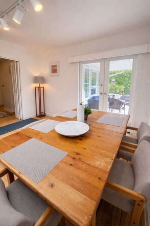 Une table de salle à manger en bois, accompagnée de quatre chaises, une assiette ronde blanche et un lampadaire.