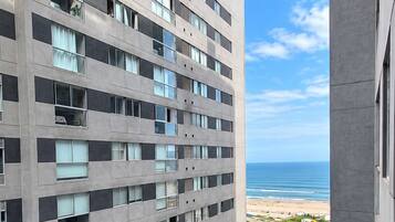 Un edificio de gran altura con varios pisos, una entrada protegida por un portón y vista a la playa y al océano.