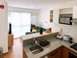 Cocina moderna con microondas integrado, fregadero y estufa. Hay una zona de comedor con un sofá verde y un jarrón de flores.