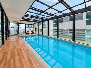 Ein moderner, überdachter Innenpool mit Holzboden und Blick auf die Stadt.