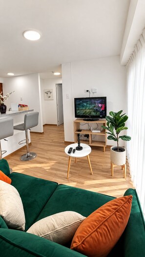 Ein modernes Wohnzimmer mit einem grünen Sofa, einem Fernseher und einem kleinen Tisch mit einer Fernbedienung.