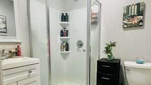 A bathroom with a glass shower enclosure, a white sink, a black cabinet, a toilet, and a small plant. - Cozy 1-bedroom apartment in nice Houston with AC (Houston)