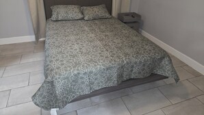 A bed with a patterned bedspread, a nightstand with a drawer, and a curtain. - Cozy 1-bedroom apartment in nice Houston with AC (Houston)