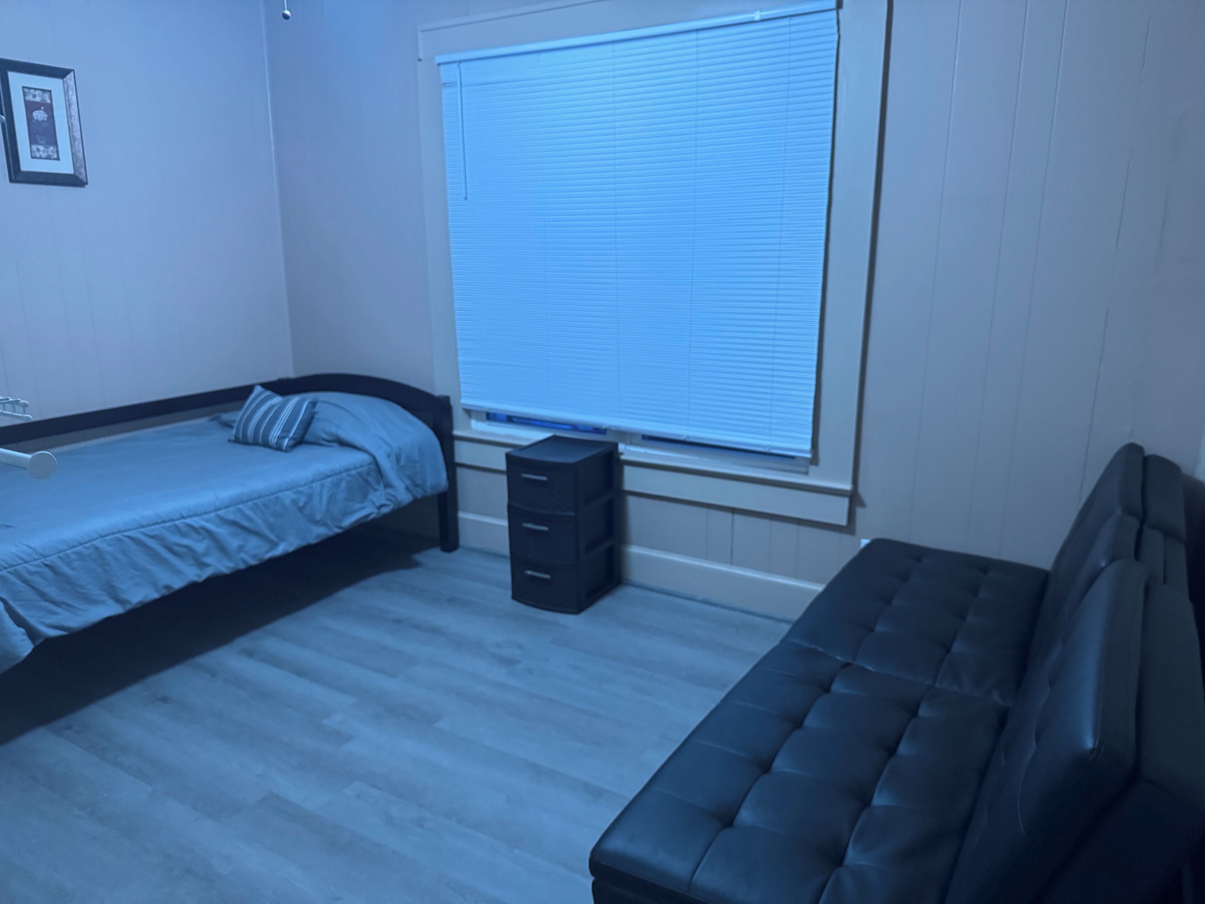 A bedroom with a bed, a dresser, and a window with blinds.