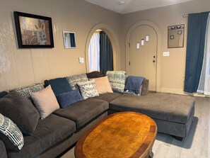 A living room with a sectional sofa, a wooden coffee table, and a door with a mirror.