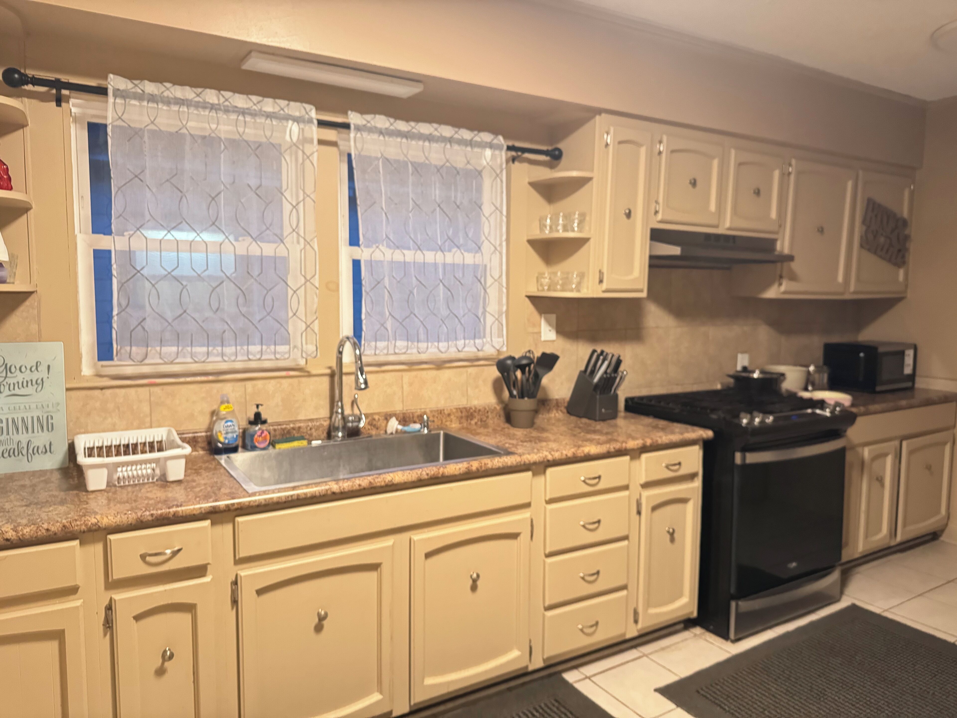 Una cocina con armarios color beige, una estufa negra, un fregadero y un microondas.