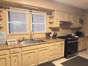 A kitchen with beige cabinets, a black stove, a sink, and a microwave.