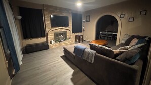 A living room with a fireplace, a sofa, a coffee table, and a dining area visible through an archway. - Large, comfortable home, great location, 4 bedroom, washer/dryer, pet friendly (Mobile)