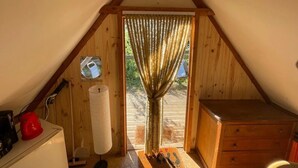 Una habitación acogedora en el ático con techo de madera, una ventana pequeña con cortinas, un armario de madera y un radiador.