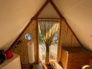 Ein gemütliches Dachzimmer mit Holzbalkendecke, einem kleinen Fenster mit Vorhängen, einem Holzschrank und einer Heizung.