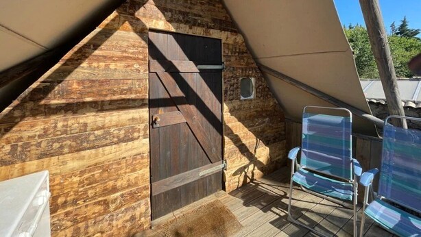 Una cabaña de madera con techo inclinado, una puerta y dos sillas.