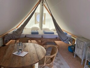 Una carpa acogedora con una cama, una mesa con un farol, sillas de mimbre y un armario de madera.