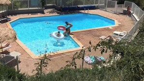 Una piscina rectangular con un deck amurallado, rodeada de vegetación y colinas al fondo.