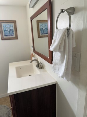 Une salle de bain avec un lavabo blanc, un meuble en bois, un miroir et une serviette suspendue à un porte-serviettes en métal.