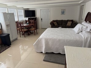 Une chambre à coucher avec un lit, un canapé, une table à manger avec des chaises, un téléviseur et une porte.