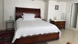 A bedroom with a wooden bed, white bedding, a nightstand with a lamp, a bedside table, and a red patterned rug. - LA JOLLA PRIVATE STUDIO (San Diego)