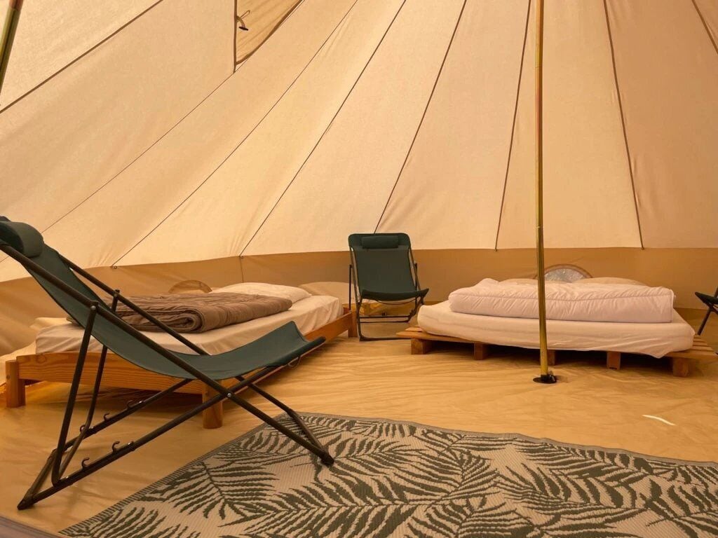 Een tent met twee bedden, een lounge stoel en een tafeltje.