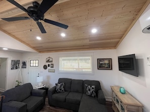 A living room with a ceiling fan, a sofa, a TV, and a window with blinds.