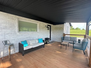 A covered patio with a white brick wall, a sofa with blue cushions, a small table, and a chair.