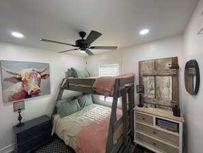 A bunk bed room with a ceiling fan, a painting of a bull, a rustic door, and a dresser. - Cozy and beautiful countryside  2-bedroom cottage in pleasant Tuscumbia with AC. (Tuscumbia)