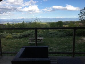 Eine Terrasse mit Blick auf eine grüne Landschaft, eine Holzbank und ein Metallgeländer.