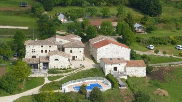 Un ensemble de bâtiments en pierre comprenant plusieurs structures, une piscine et des espaces verts environnants.