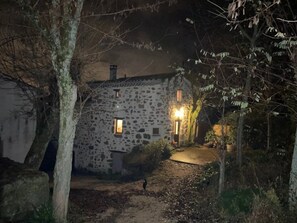 Ein Steinhaus mit einem Feldweg, der davor hindurchführt, umgeben von Bäumen.