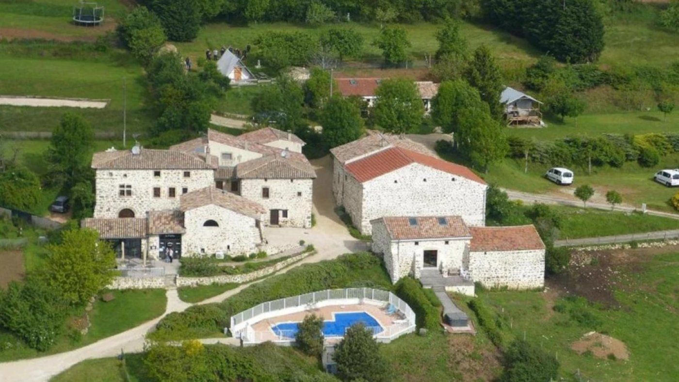 Un complejo de edificios de piedra con varias construcciones, una piscina y abundante vegetación.