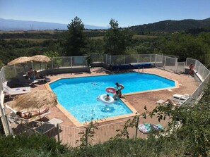 Ein Schwimmbad mit Blick auf die Landschaft, umgeben von Liegestühlen und einem Zaun.