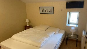 A bedroom with a bed, a nightstand, a lamp, a window, and a radiator. - Camping 3 étoiles - Piscine  - ccbgcdg (Plats)