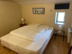 Ein Schlafzimmer mit Bett, Nachttisch, Lampe, Fenster und Heizkörper.