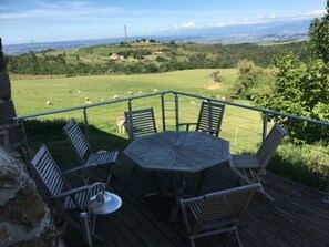 Eine Terrasse mit Tisch und Stühlen mit Blick auf ein grasbewachsenes Feld mit Schafen.