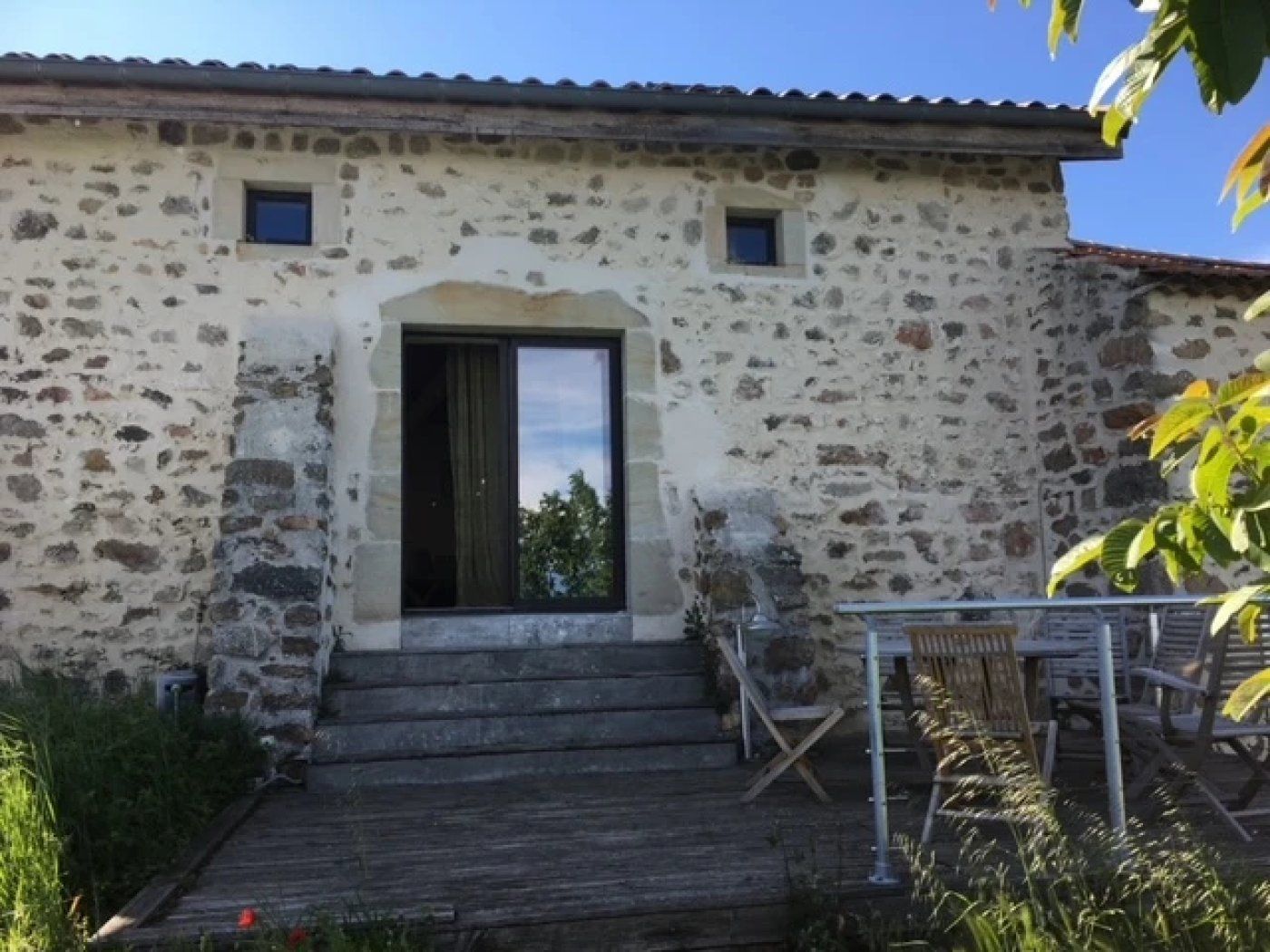 Un bâtiment en pierre avec un escalier en bois menant à une porte, des sièges à l’extérieur et un ciel dégagé.