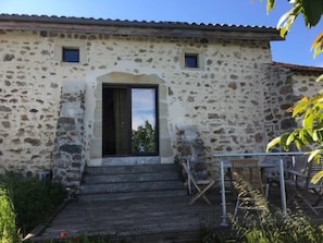 A stone building with a wooden staircase leading to a door, outdoor seating, and a clear sky. - Camping 3 étoiles - Piscine  - ccbgcdh (Plats)