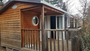 Eine Holzhütte mit einer Terrasse, einem Rundfenster und einer Tür.