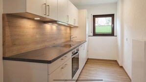 Eine kleine Küche mit Holzausstattung, einer Edelstahlspüle und einem Fenster mit Jalousien.