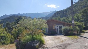 Un petit bâtiment avec une allée de gravier, entouré de verdure et avec des montagnes en arrière-plan.